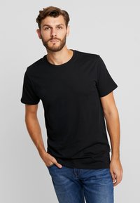 Black cotton t-shirt with short sleeves and a round neckline. Model wears it with blue jeans, displaying a relaxed fit and smooth texture.