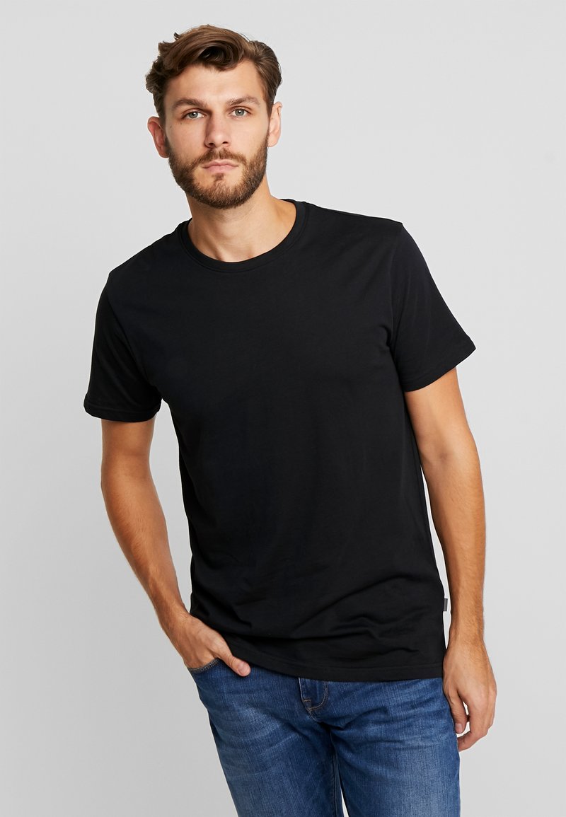 Black cotton t-shirt with short sleeves and a round neckline. Model wears it with blue jeans, displaying a relaxed fit and smooth texture.