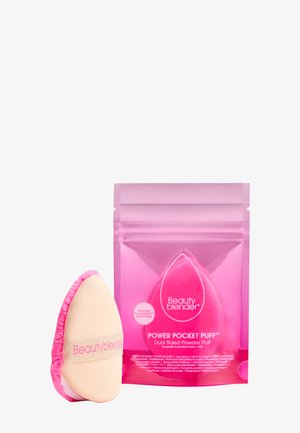 Dubbel-sidig puder puff med en tan-färgad framsida och rosa kant, förpackad i en rosa transparent påse med vit text och varumärke.