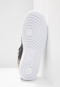 Sneaker nera con decorazioni a forma di stella dorata, con suola in gomma bianca caratterizzata da motivi a cerchi concentrici e bordi testurizzati.