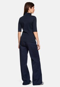 Navyblauw kort mouwen top met hoge kraag, gecombineerd met losvallende donkere denim broek. Glad textuur, casual ontwerp.