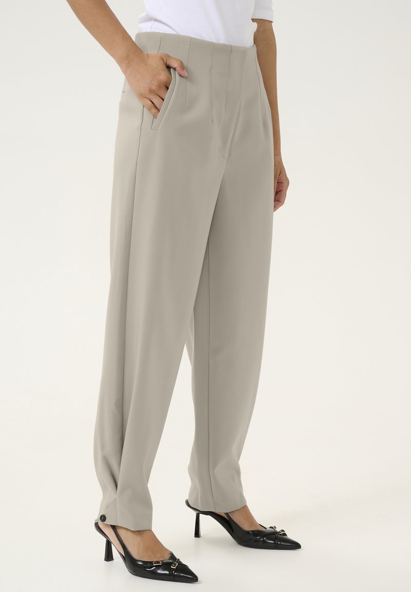 Krémové kalhoty s vysokým pasem a rovnou siluetou, s bočními kapsami a švy s knoflíky na lemování, v kombinaci s černými lodičkami se špičatou špičkou.