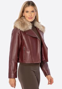 Veste en cuir bordeaux courte avec un col en fausse fourrure, dotée d'une fermeture éclair asymétrique et de poches latérales. Texture lisse avec un design ajusté.