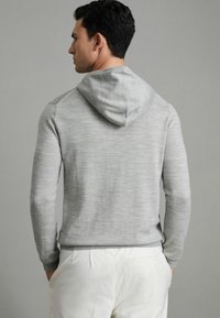 Grauer Hoodie mit weichem Material, ausgestattet mit einer Kapuze mit Kordelzug, gerippten Bündchen und einer schlanken Passform, kombiniert mit cremefarbenen Hosen.