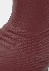 Raudona guminė boot su tekstūruota, šešiakampio rašto paviršiumi. Pasižymi raitytomis detalėmis palei pagrindą, kad pagerintų sukibimą.