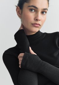 Top a collo alto nero a costine con maniche lunghe aderenti e polsini senza dita. Texture liscia e design attillato che evidenziano l'eleganza.