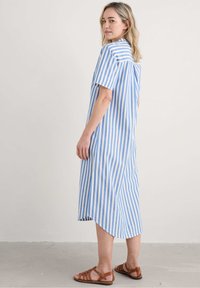 Abito camicia a righe blu e bianche con maniche corte, lunghezza al ginocchio, tessuto leggero, orlo arrotondato e dettaglio dello yoke posteriori con bottoni.