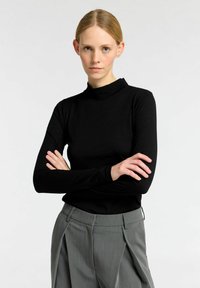 Zwarte lange mouw mock neck top gemaakt van zachte stof, gecombineerd met grijze geplooide broek met een soepele textuur en een getailleerde pasvorm.