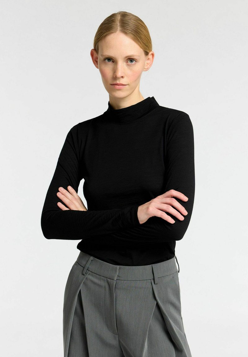 Zwarte lange mouw mock neck top gemaakt van zachte stof, gecombineerd met grijze geplooide broek met een soepele textuur en een getailleerde pasvorm.
