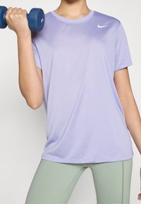 Camiseta deportiva morada hecha de tejido suave, con cuello redondo y mangas cortas, combinada con leggings verde claro y un manillar azul.