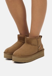 Stivali alla caviglia in suede beige con punta arrotondata, tacco basso e cuciture decorative. Presenta una morbida fodera interna e una suola in gomma testurizzata.