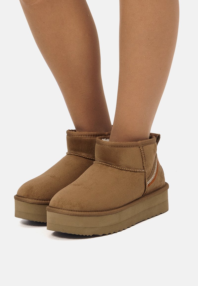 Stivali alla caviglia in suede beige con punta arrotondata, tacco basso e cuciture decorative. Presenta una morbida fodera interna e una suola in gomma testurizzata.