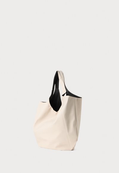 Beżowa torba na ramię z czarnymi uchwytami, wykonana z gładkiego, teksturowanego materiału. Posiada przestronną wnętrze i minimalistyczny design.