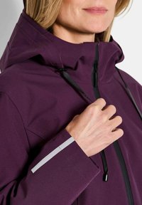 Paarse waterdichte jas met een hoge kraag, verstelbare trekkoorden en reflexaccenten op de mouwen voor zichtbaarheid.