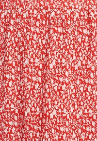 Tissu rouge avec un motif floral blanc, présentant une texture plissée et des plis, créant une apparence légère et aérée.