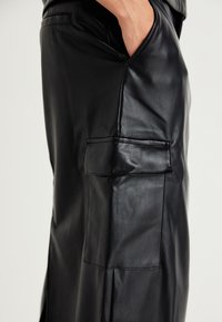 Schwarze Lederhose mit schlanker Passform, ausgestattet mit Seitentaschen und einer einzelnen Gesäßtasche, die eine glatte Textur und ein elegantes Design präsentieren.