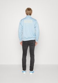 Felpa Nike azzurro chiaro con collo alto, polsini a costine e un grande logo sulla schiena. Abbinata a jeans neri e sneaker blu.