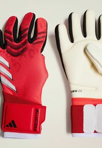 Guanti da portiere rossi con superficie grip testurizzata, accenti neri e fasce da polso regolabili con marchio "Predator".