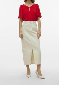 Rød kortærmet bluse med nøglehul-detalje, parret med en lang cremefarvet nederdel med en frontal slids og beige højhælede sko.