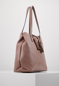 Sac fourre-tout en cuir rose avec des glands, design spacieux, fond plat et doubles anses d'épaule. Texture lisse et forme structurée.
