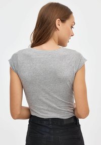 Camiseta gris de manga corta con cuello redondo, textura suave, de estilo ajustado, exhibida desde la parte de atrás junto a unos pantalones vaqueros negros con bolsillos.