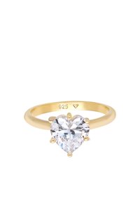 Anello placcato in oro con una pietra preziosa trasparente a forma di cuore, caratterizzato da sei griffes e una fascia liscia. All'interno della fascia è impresso "925" per indicare la qualità dell'argento.