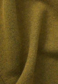 Tessuto di lana di colore verde oliva, con una consistenza morbida e una leggera lucentezza. Il materiale si drappeggia in modo fluido, mostrando un motivo sottile e coerente.