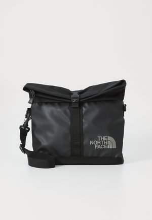 Schwarze Rolltop-Tasche aus wasserdichtem Material, mit stabilen Gurtbändern, einem in Silber geprägten Logo und einem eleganten Design.
