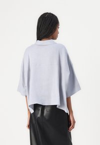 Top in lino azzurro chiaro con vestibilità rilassata, maniche corte, dettaglio sulla spalla posteriore e orlo asimmetrico, abbinato a una gonna in pelle nera.
