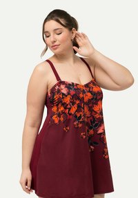 Zwemjurk voor zwangerschappen in bordeauxrood met een oranje bloempatroon. Voorzien van verstelbare bandjes en een relaxte pasvorm, gemaakt van zacht zwemmateriaal.
