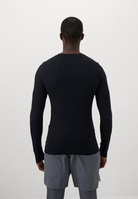 Camisola atlética preta de manga longa com um design ajustado, textura suave e mangas raglan, usada com calções desportivos cinzentos.
