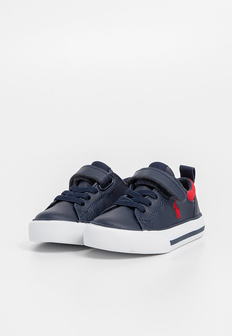 Baskets en cuir bleu marine avec une semelle en caoutchouc blanche, dotées de lacets et d'une sangle en velcro, rehaussées d'un logo rouge sur le côté.