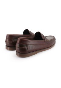 Mocasines de cuero marrón con una textura suave, que presentan detalles cosidos y un diseño elevado en el talón. Suela de goma.