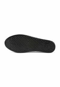 Semelle de chaussure en caoutchouc noir présentant un motif texturé de petits points arrondis pour l'adhérence, avec un logo circulaire à une extrémité.