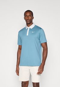 Šviesiai mėlyna Nike polo marškinėliai su balta apykakle. Trumpomis rankovėmis ir subtiliu logotipu krūtinėje. Lygus audinio paviršius ir laisvas kirpimas.