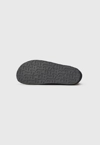 Suela de zapato de goma negra con un patrón de textura, que presenta surcos y letras en relieve para mejorar el agarre. Sin marcas ni adornos visibles.