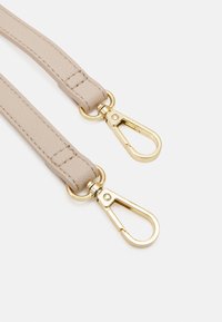 Beige läderrem med guldmetallspännen i varje ände. Remmen har en texturerad yta och är sydd längs kanterna.