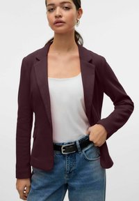 Bordový blazer se strukturovaným designem, límečkem a zapínáním na jeden knoflík, vrstvený přes bílý top a kombinovaný s džíny s vysokým pasem.