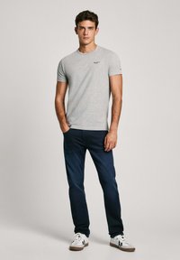 Hall sõlgadega hall t-särk ümmarguse kaelusega, kantud tumedate siniste teksadega. Särk on kaunistatud väikese logoga vasakul rinnal ja valgete tossudega.