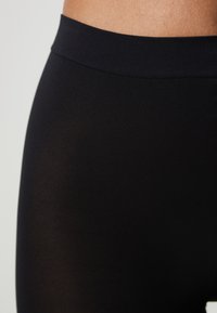 Svarta leggings med en slät yta och en bred, platt midja. Tyget verkar ogenomskinligt med en tajt, åtsittande design.