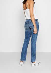 Světle modré denimové džíny s rovnými nohavicemi a jemným vyblednutím. Nosené s jednoduchým bílým tričkem a bílými teniskami. Viditelné zadní kapsy.