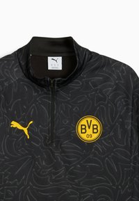 Chaqueta deportiva negra con cremallera hecha de tela texturizada, que presenta un patrón sutil, un logo de Puma amarillo y un distintivo circular de Borussia Dortmund.