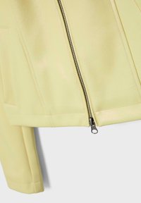 Light yellow jacket section showing a silver zipper and stitched seams on smooth fabric with part of a sleeve visible.