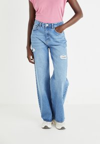 Jeansi largi de culoare albastru deschis, din denim, cu detalii rupte la genunchi, talie cusută și un fit relaxat.