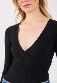 Top de manga longa preto com uma design de decote em V profundo, apresentando um estilo envolvente e tecido texturizado.