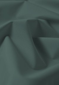 Weicher dunkelgrüner Stoff mit subtilem Gittermuster, Nahaufnahme mit sanften Falten und Schatten, die Tiefe erzeugen.