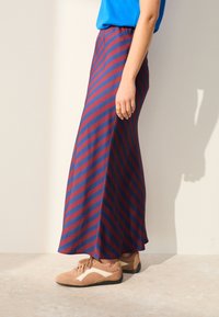 La gonna lunga presenta strisce orizzontali rosse e blu navy, tessuto morbido, forma a trapezio e vita elastica; abbinata a sneaker marrone chiaro.