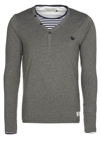 Maglietta henley grigia a maniche lunghe con tre bottoni e maglietta a righe blu navy e bianca visibile all'collo e ai polsini.