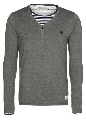 Maglietta henley grigia a maniche lunghe con tre bottoni e maglietta a righe blu navy e bianca visibile all'collo e ai polsini.