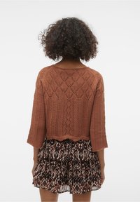 Brązowy dziergany sweter typu crop z wzorem diamentów i rękawami 3/4, w zestawie z wzorzystą spódnicą z falbankami w ziemistych odcieniach.